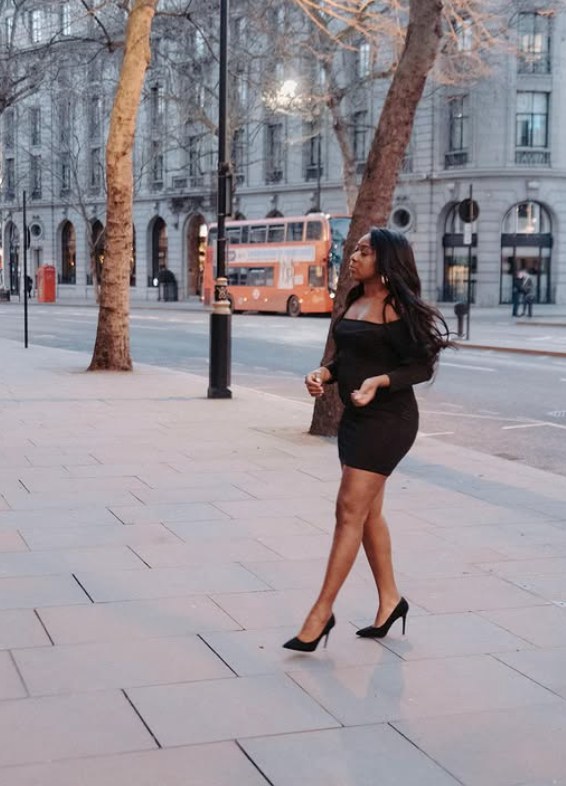Marcelle Adrianna walking a central London street at dusk in a black mini dress and heels.