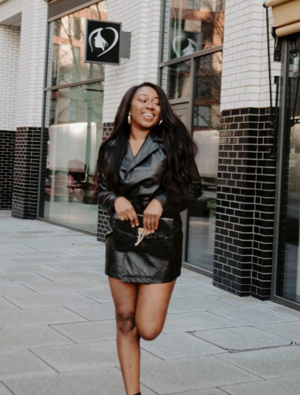 Marcelle Adrianna walking in a black leather mini dress with a clutch, London street.